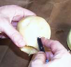 a person's hands carving a face into a peeled apple