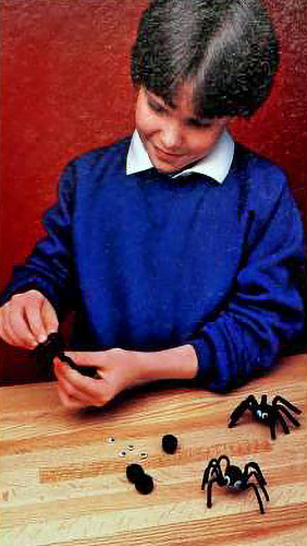 a boy in 1980s-style clothes assembles a pipe-cleaner spider