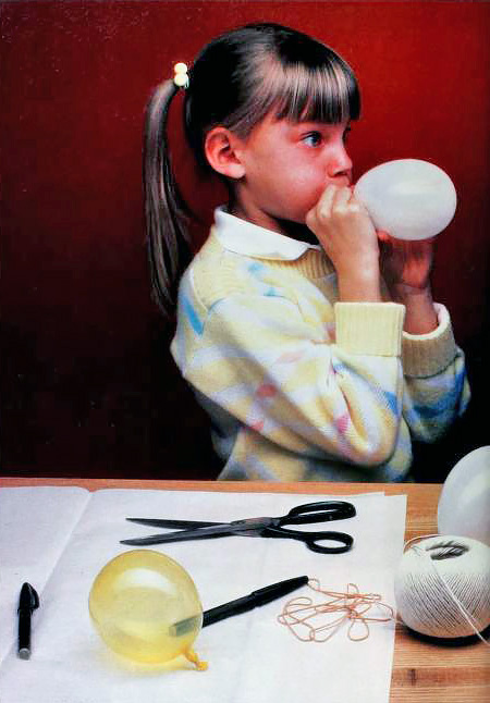 a girl in 1980s-style clothing blows up a small balloon
