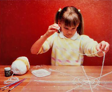 a girl in 1980s-style clothing assembles string-and-glue spiderwebs