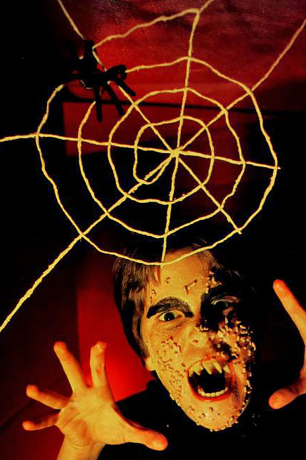 a boy in homemade monster makeup poses menacingly beneath a string-and-glue spiderweb