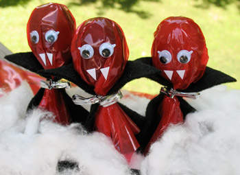 a photo of lollipops wrapped in red cellophane, dressed in black capes with white fangs, to resemble vampires